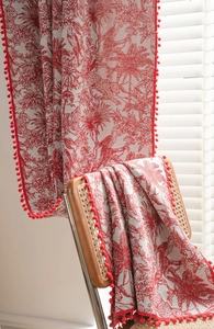 Detail of red toile de jouy pattern curtains with pompom fringe on a wooden chair