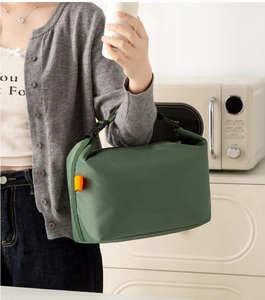 Detail of green insulated lunch bag with orange label and buckle handle in a kitchen