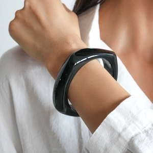 Close-up of a minimalist chunky black acrylic bangle with a polished geometric profile