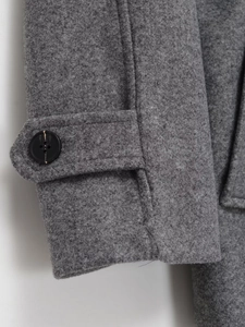 Detail shot of grey woolen coat cuff showing premium fabric texture and button strap