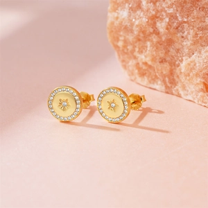 Detail of gold starburst stud earrings with white zircons on a pink stone background