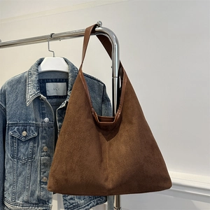 Brown suede leather tote bag hanging on a rack with a denim jacket background