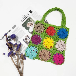 Detail of handmade crochet handbag with colorful floral patterns on green knit base