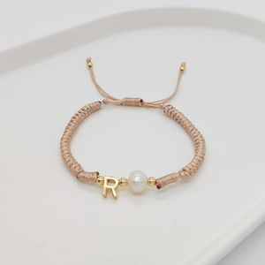 Detailed macro view of handmade braided gold rope bracelet with letter R and pearl charm
