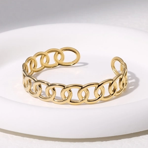 Dettaglio di un bracciale dorato a catena traforata su un vassoio bianco pulito