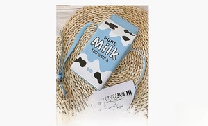 Detail view of milk carton shaped crossbody bag on a woven mat with pure milk print