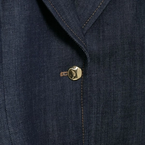 Dettaglio giacca in denim blu scuro con cuciture a contrasto e bottoni in metallo oro