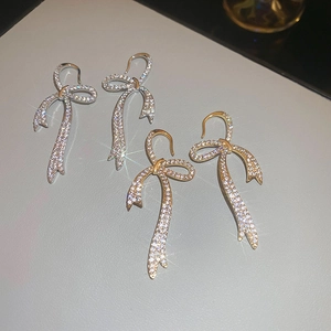 Detailed view of gold and silver bow earrings with pave-set shimmering zircon stones