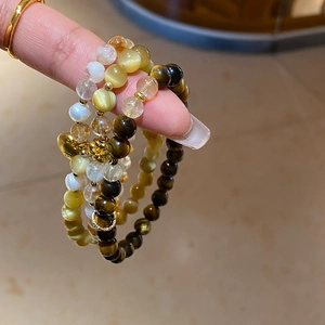 Détail macro de bracelets superposés en œil de tigre et perles avec breloques cœur dorées