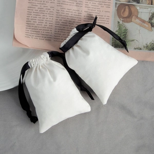 Detailed view of white cotton drawstring jewelry pouches with elegant black ribbons