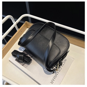 Close-up of a black leather crossbody bag featuring gold hardware and a rolled shoulder strap