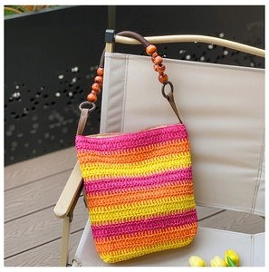 Close-up of rainbow straw tote bag with wooden bead straps on a canvas chair