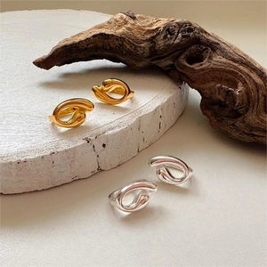 Artistic display of curved minimalist metal rings on white stone with dry wood accents