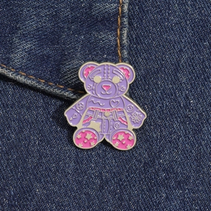 Close-up of a purple enamel bear brooch with street art symbols on denim fabric