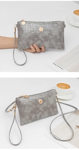 Detail view of a grey crocodile embossed crossbody clutch bag with gold hardware