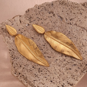 Macro detail of golden feather leaf earrings with fine texture on a natural stone base