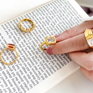 Close-up of four gold rings with red and clear square zircon stones on book pages