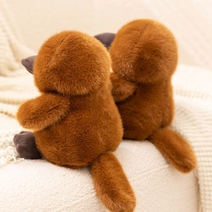 Rear view of cute brown plush platypus toys showing soft fluffy texture on a cozy blanket