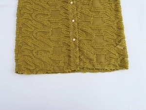 Detail of mustard yellow blouse with textured fringe fabric and pearl buttons
