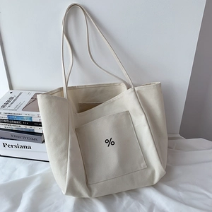 Close-up of cream canvas tote bag featuring front pocket and minimalist percent logo