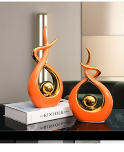Close-up of modern orange ceramic sculptures with gold accents on a black reflective surface