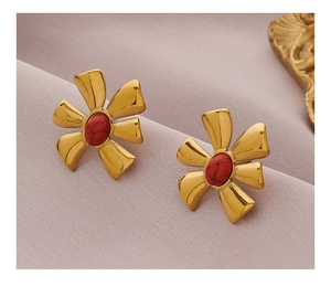 Detail of flower-shaped golden earrings with red natural stone inlays on fabric