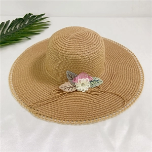 Detail of a wide-brimmed straw hat with delicate floral lace and fabric leaf ornaments
