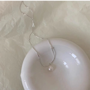 Detailed macro view of a silver bead chain with a teardrop pearl pendant on a dish