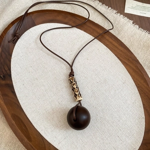Macro view of vintage round wood pendant with gold filigree bead on brown cord chain