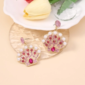 Detailed close-up of shell-shaped earrings with pink rhinestones and white pearls on glass