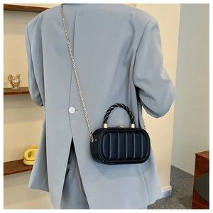 Close-up of a black textured box bag with gold chain and woven handle on a blue blazer