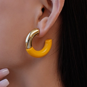 Model wearing gold and yellow C-shaped acrylic earrings with a minimalist metal accent