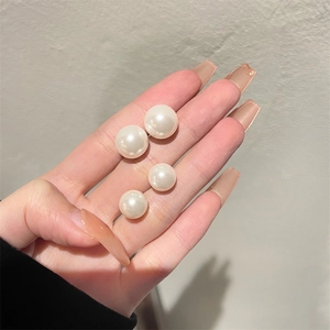 Detail shot showing two pairs of white pearl earrings in different sizes held by hand