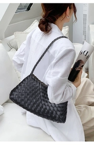 Detailed view of the black woven leather shoulder bag worn by a model in a minimal setting