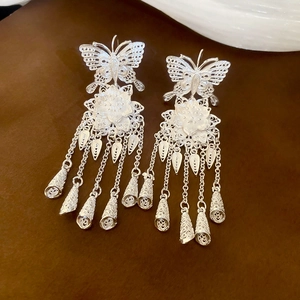 Macro detail of silver tassel earrings with hollow butterfly and flower design motifs