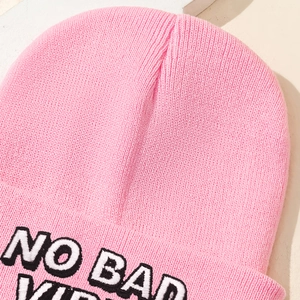 Detailed close-up of pink knit beanie with white NO BAD VIBES embroidery texture