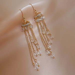 Detail of elegant gold tassel earrings with clear crystal beads on champagne silk background