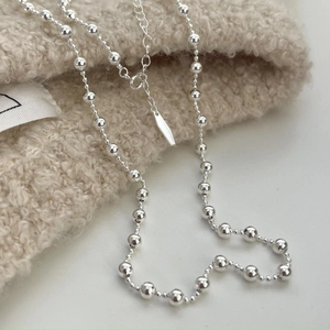 Close-up of minimalist silver bead necklace with lobster clasp on soft fabric