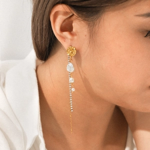 Close-up of golden tassel earrings featuring irregular pearls and shimmering zircon chains