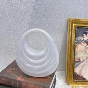 Artistic detail of wavy white acrylic handbag resting on a vintage book and fur mat