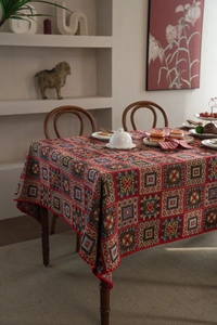 Close-up of red geometric jacquard tablecloth with tassel fringe on a wooden dining table
