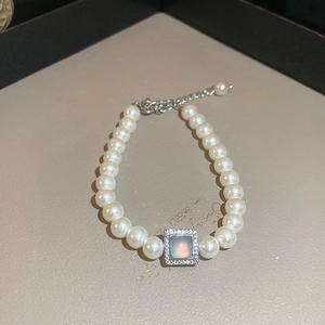 Détail d'un bracelet en perles avec un pendentif carré en cristal au centre iridescent