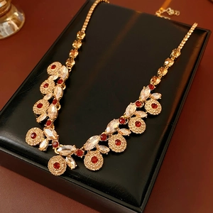 Detailed view of a vintage gold necklace with red crystals on a black leather jewelry box
