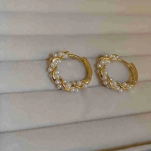 Detail of twisted gold metal hoop earrings with white pearls on a beige jewelry tray