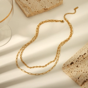 Detail view of gold layered paperclip and link chain necklaces on a beige aesthetic background