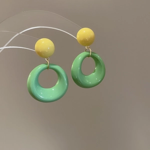 Detail of green resin hoop earrings with yellow sphere stud and golden metal connectors