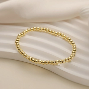 Minimalist gold beaded elastic bracelet with heart key pendant on white silk fabric