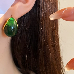 Close-up of emerald green teardrop resin earring on ear with golden metal frame