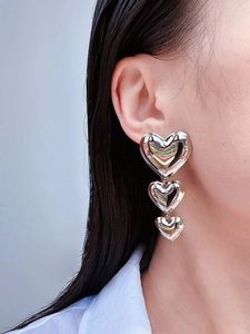 Gros plan de boucles d'oreilles pendantes triple cœur argentées au fini brillant