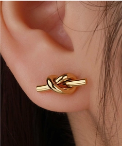 Close-up of minimalist gold knotted stud earring worn on ear with polished finish